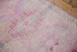 Distressed Oushak runner, low pile, showing pink ram's horn and diamond border motifs.