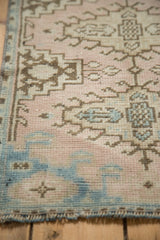 Vintage distressed Oushak rug with low pile, blush pink, sky blue, and brown geometric motifs.