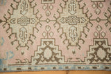 Distressed Oushak rug edge showcasing geometric motif in blush, sand, and chocolate.