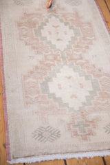 Distressed Oushak rug with faded ivory, rose, and pale sage geometric patterns and fringe.