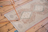 Corner of distressed Oushak rug with faded ivory, silver, and burgundy geometric pattern.