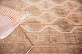 Distressed vintage Afghan carpet showing blush, brown geometric gul pattern and low pile.