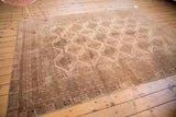 Distressed vintage Afghan rug corner, revealing faded brown and blush borders with geometric gul motifs.
