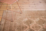 Distressed Afghan carpet corner showing low pile, muted blush, and coffee brown patterns.