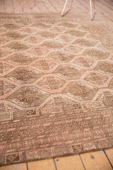 Distressed Afghan carpet's blush and brown repeating gul motifs and intricate geometric border.