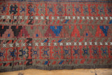 Geometric serrated patterns of antique Belouch rug in cherry red, navy, and earthy tones.