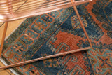 Distressed Veece rug close-up: low pile, exposed knot heads, dusty teal, and burnt orange.