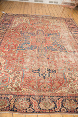 Localized wear revealing cherry red, navy blue, and ivory geometric patterns on a vintage Heriz rug.