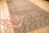 Distressed Khotan carpet showing blush pomegranate motifs, braided border, and wear to knot heads.