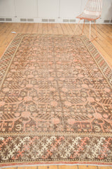 Distressed vintage Khotan carpet's intricate braided border with pink pomegranate motifs.