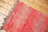 Faded cherry red long pile texture revealing light foundation threads and dark fringe.
