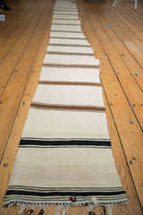 End of the vintage Turkish Kilim runner with horizontal ivory, coffee, and black banded stripes and frayed edge.