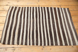 Secured side edge of a vintage Turkish Kilim rug, with charcoal and ivory banded stripes.