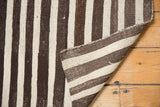 Folded vintage Turkish Kilim rug showing hand woven striped texture in charcoal brown and ivory, with a secured edge.