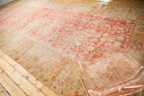 Distressed corner of antique Khotan carpet, with faded cinnabar red, ivory, and gold patterns.