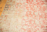 Faded cinnabar red and ivory patterns on distressed Khotan carpet with mostly even wear.