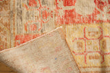 Corner showing distressed Khotan pile with faded cinnabar, ivory, and visible hand-knotted foundation.
