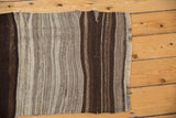 Fringed end of hand-woven Turkish Kilim rug showing oblique gray and brown bands.