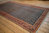 Angled view of the vintage Malayer carpet, with navy field, allover red paisley boteh, and floral borders.