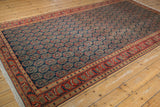 Corner of a Vintage Malayer carpet, showing fringe, orange-red floral border, navy boteh field.