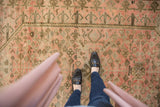 Distressed vintage Oushak carpet with worn pile, blush hues, and intricate faded patterns.