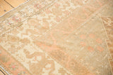 Worn Oushak rug corner, featuring faded floral motifs and stylized borders in gold, ivory, and blush.
