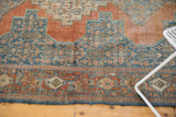 Distressed vintage Persian Senneh rug with intricate Herati motif, geometric border, terracotta, and denim blue.