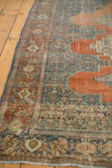 Distressed vintage Senneh rug's intricate blue Herati field and terracotta medallion contour.