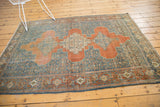 Distressed vintage Senneh rug corner showing terracotta border and intricate blue Herati field.
