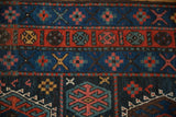 Intricate geometric floral guls in indigo, red, and dusty gold on the hand-knotted rug.