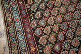 Ornate red, blue, ivory borders alongside a charcoal field of staggered boteh motifs on this antique Kurdish runner.
