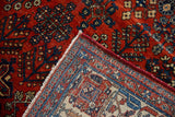 Folded corner of a distressed vintage Joshegan carpet showing ruby red pile and woven back.