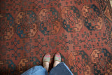 Vintage Ersari carpet with repeating chestnut, mallard green, and ivory floral medallions, showing areas of wear.