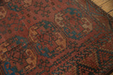 Detail of vintage Ersari carpet's zigzag border and field medallions in rust and green.