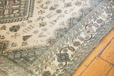 Distressed Shiraz carpet corner showcasing muted beige, dusty blue border motifs, and visible foundation.