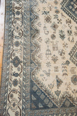 Distressed vintage Shiraz carpet, geometric border, stylized birds, dusty blue and brown tones.