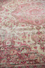 Distressed texture of a vintage Meshed rug, revealing faded pink floral motifs and foundation.