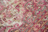Distressed vintage rug detail: raspberry, pink, ivory floral blossoms and scrolling vines with visible foundation.