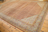 Corner view of distressed Sivas carpet with burnt orange boteh pattern and geometric blue border.