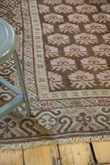 Distressed Khotan rug corner, showing faded pink floral bouquets, undulating border, and fringe.
