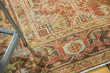 Vintage distressed Heriz carpet close-up, textured brick red and celadon geometric patterns.