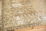 Distressed Heriz carpet corner features primitive geometric patterns in antique ivory, silver, and brown.