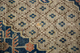Beige floral trellis field of a vintage Khotan carpet, navy blue border, older restoration.