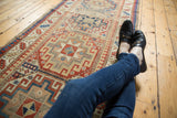 Antique Moghan Kazak runner features geometric gul medallions, brick red, sky blue, and ivory, with legs.
