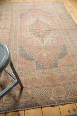 Distressed Oushak rug corner with hook motif, showing muted mauve and blue tones.