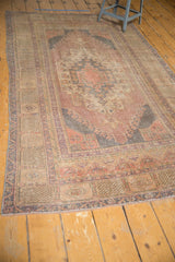 Distressed vintage Oushak rug corner with decorative hook motif and clean fringe.