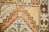 Distressed Oushak rug close-up: low pile, stepped geometric, tangerine, saffron, ivory.
