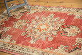 Distressed Oushak rug corner showing geometric spandrel, brick red field, and worn ivory tones.