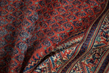 Repeating boteh pattern and striped border on a folded Mir Sarouk rug in rust, navy, ivory.