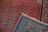 Close-up of vintage Mir Sarouk rug showing worn rust red pile and detailed geometric blue foundation.